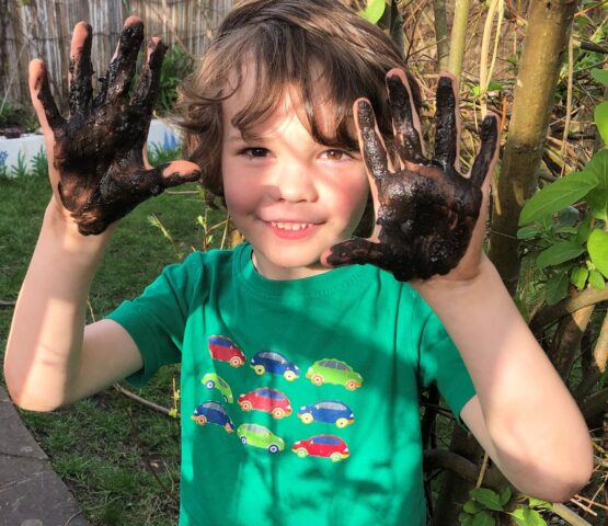 young boy smiling with muddy hands