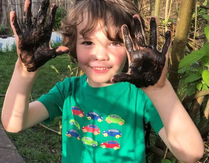young boy smiling with muddy hands