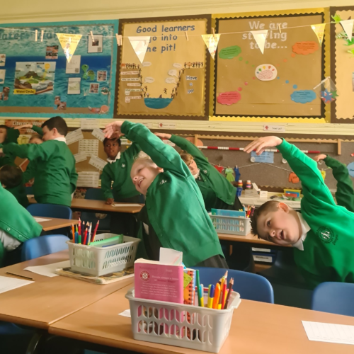 School pupils in a classroom with arms in the air