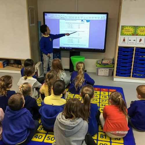 Pupil leading a lesson to his peers, stood at a the front of a class