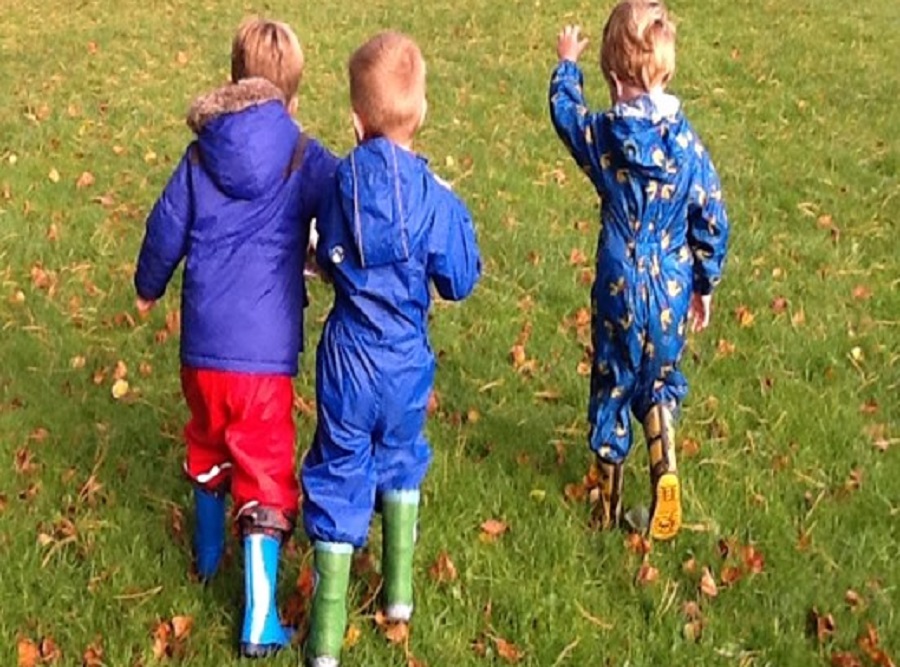 Three young learners on a field, they're wearing boots and blue coats.