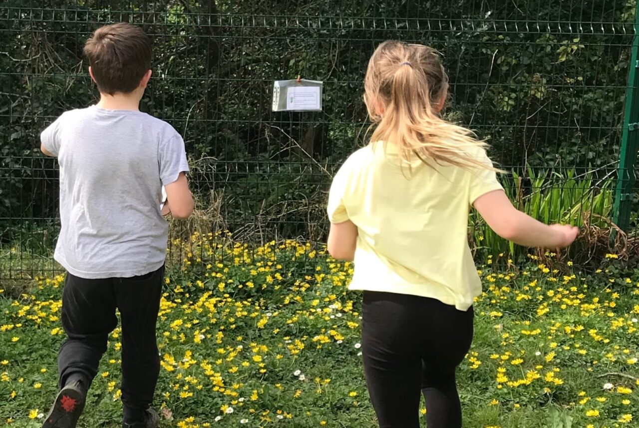 Dau berson ifanc ar gae yn cerdded tuag at ffens.
