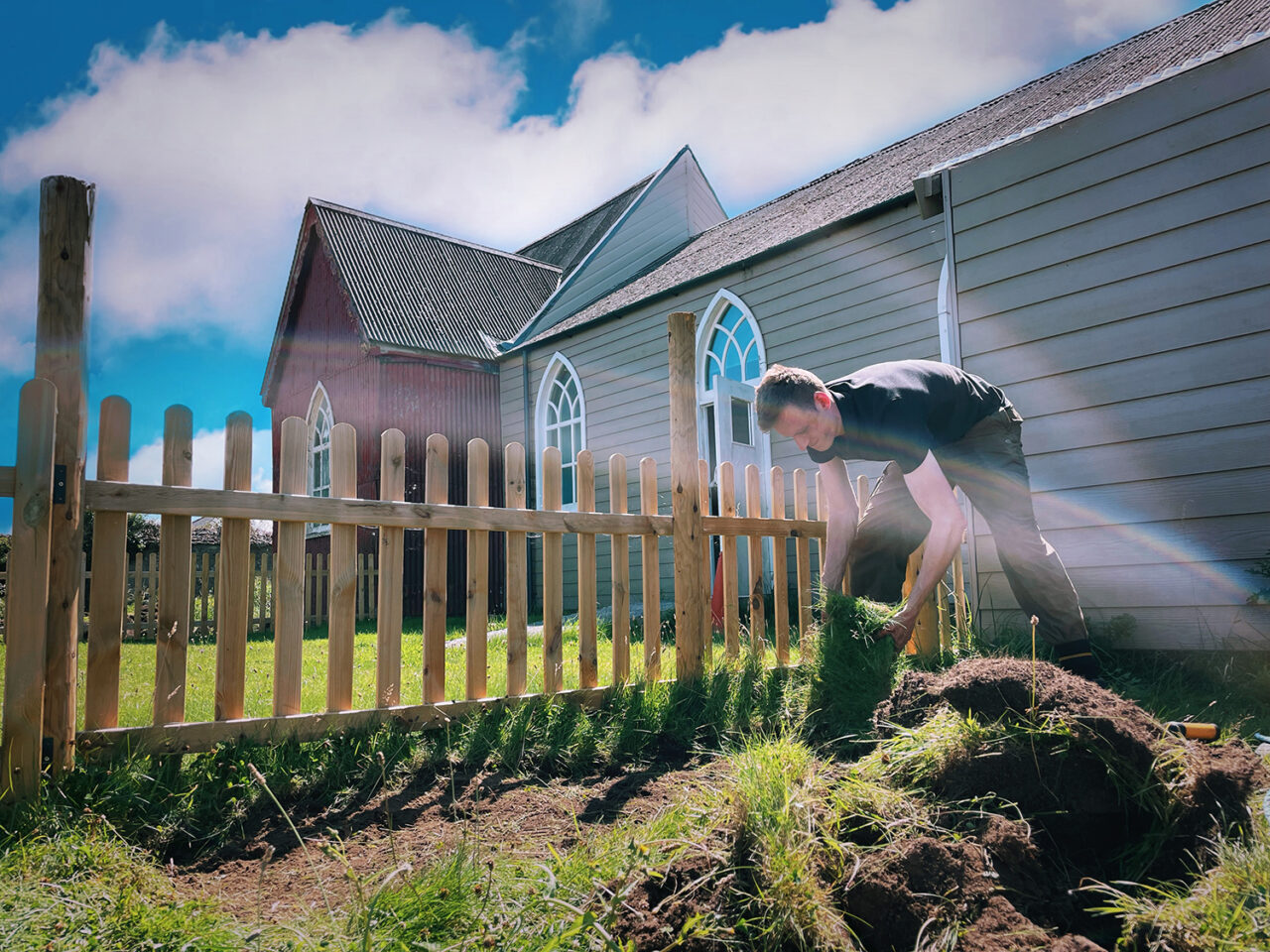 Person yn gwisgo crys-t du yn gosod glaswellt o flaen eglwys. 