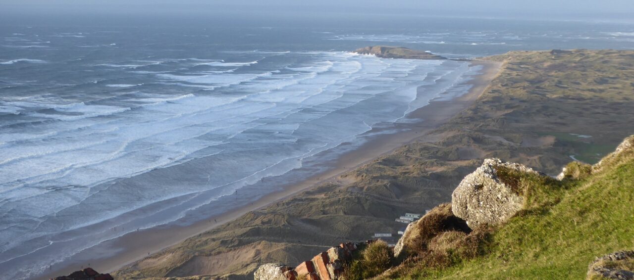 Aerial view of Rhossili beach, with waves washing up on the shore.