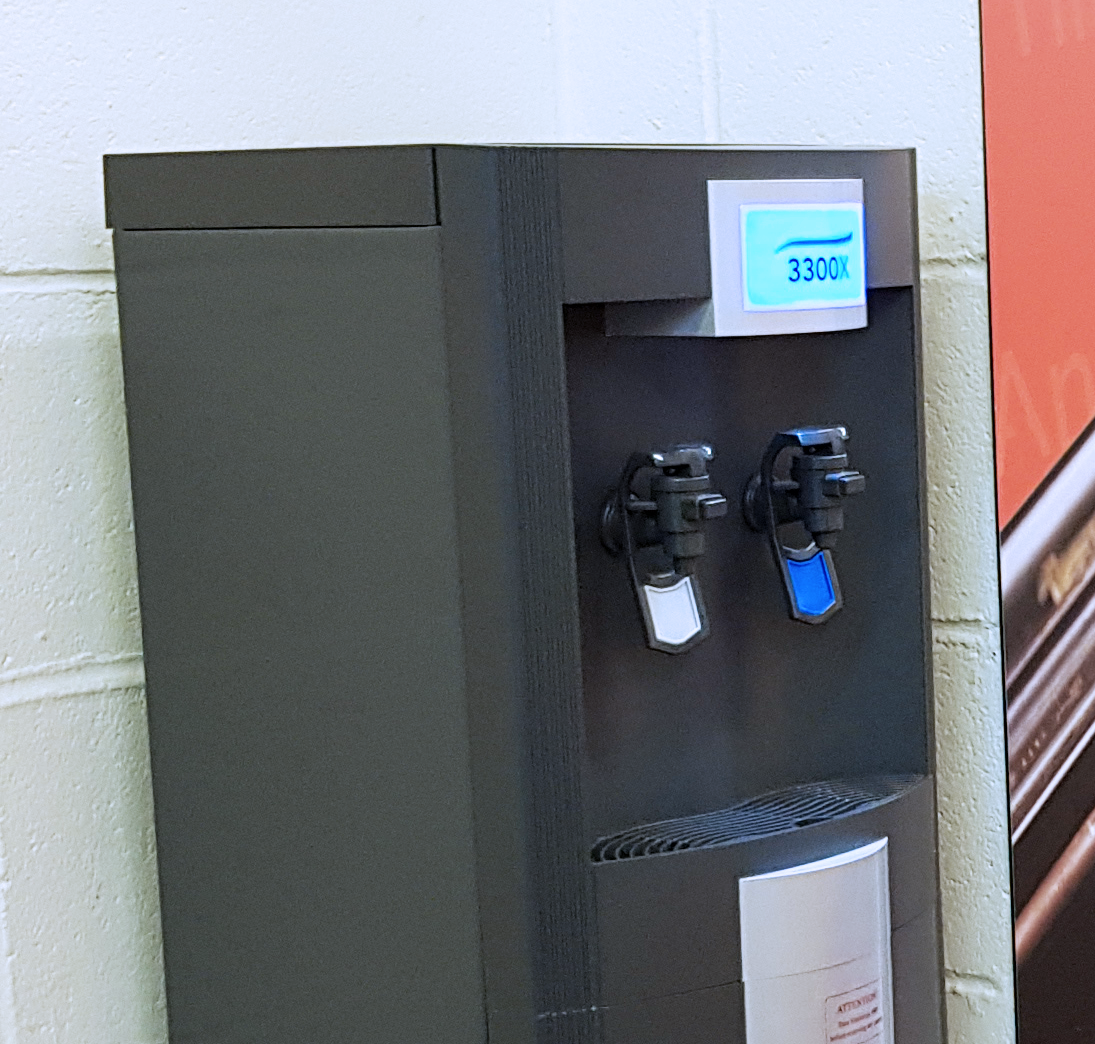 An electric water fountain next to a white brick wall.