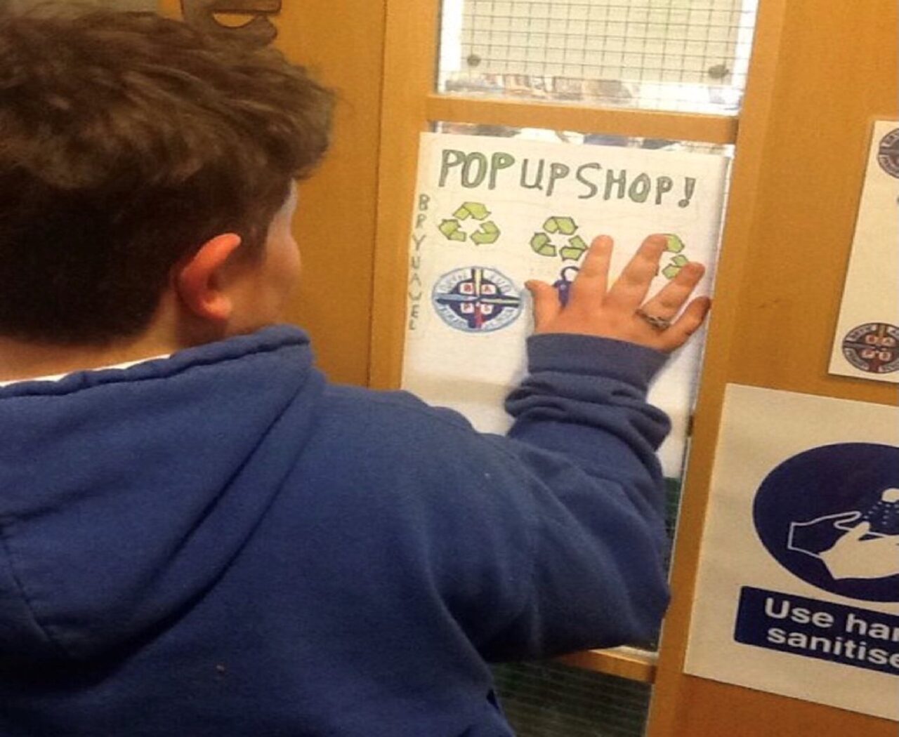 Dysgwr ifanc yn rhoi ei law yn erbyn drws, yn gwisgo gwisg las.