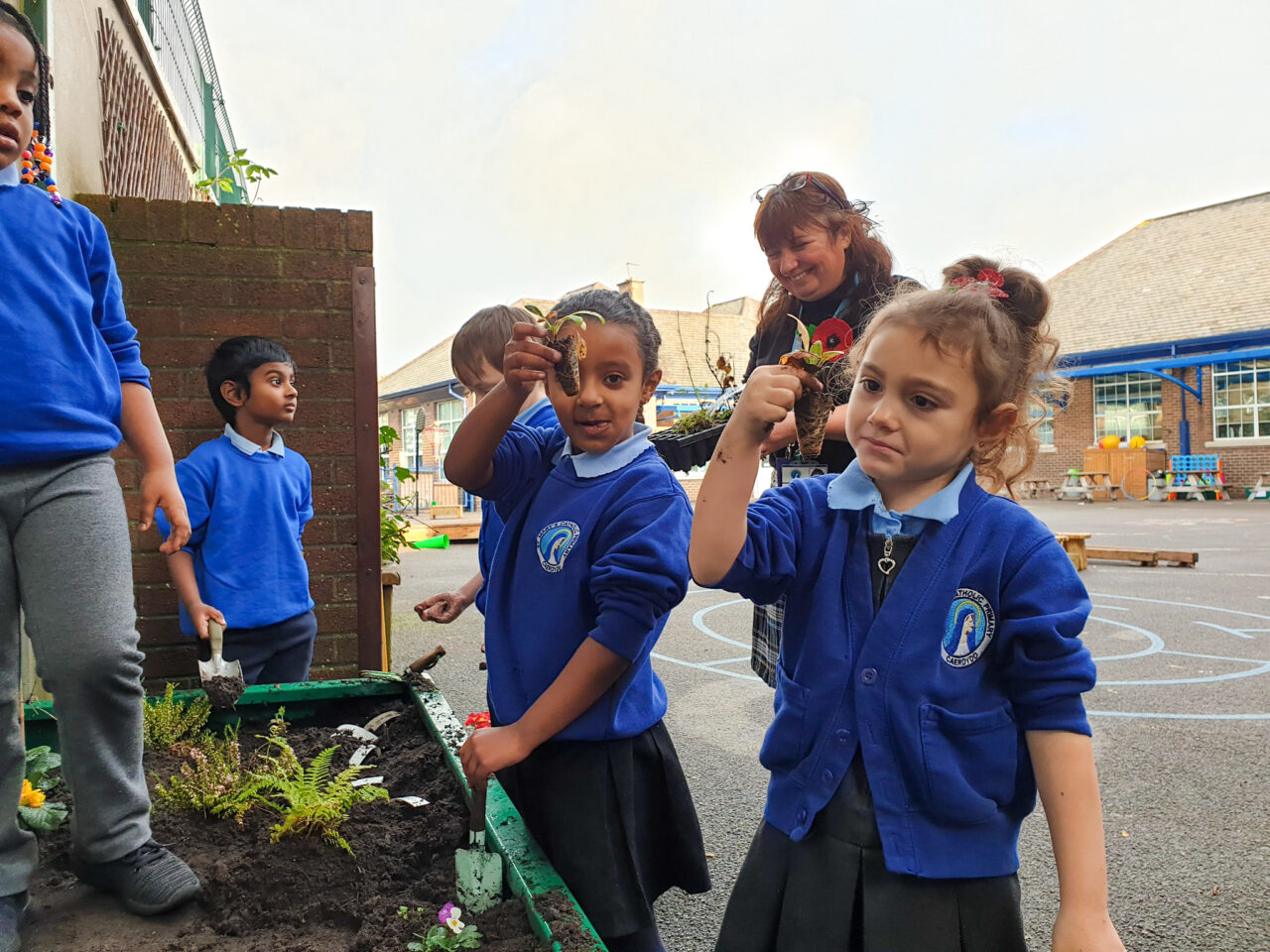 A group of young learners standing beside a raised bed, wearing blue uniform.