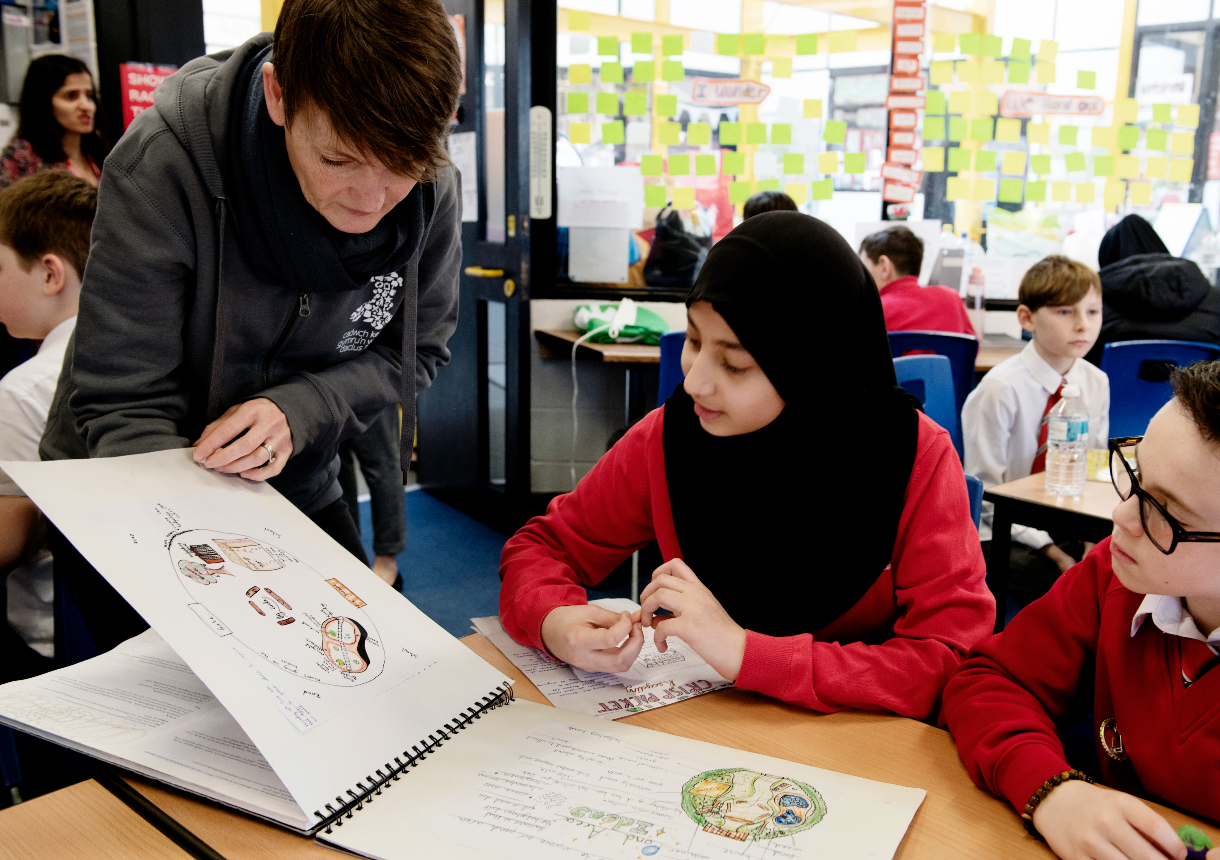 A young person reading a book of Eco ideas, wearing red uniform. There is a education officer standing alongside.