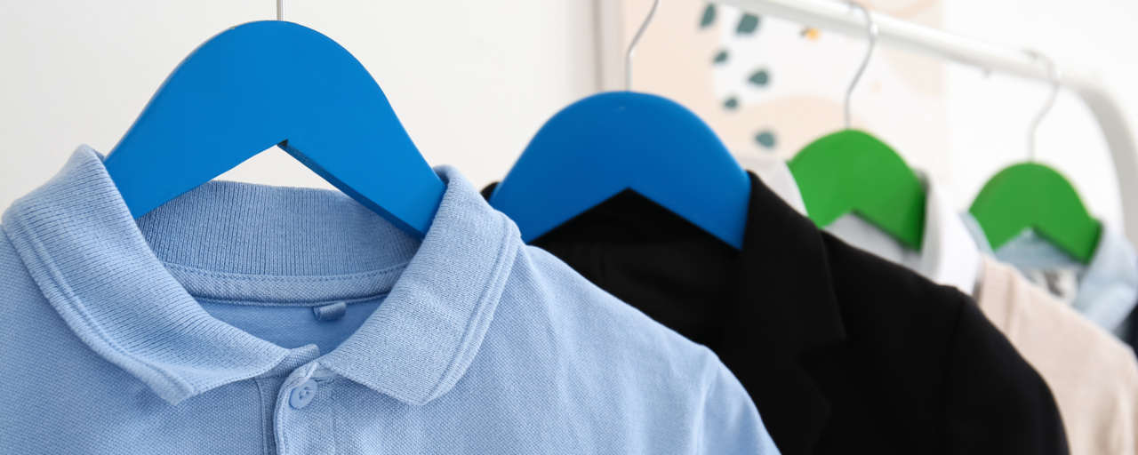 Mae crys polo glas golau a siaced ddu yn hongian ar grogfachau lliwgar ar rac dillad.