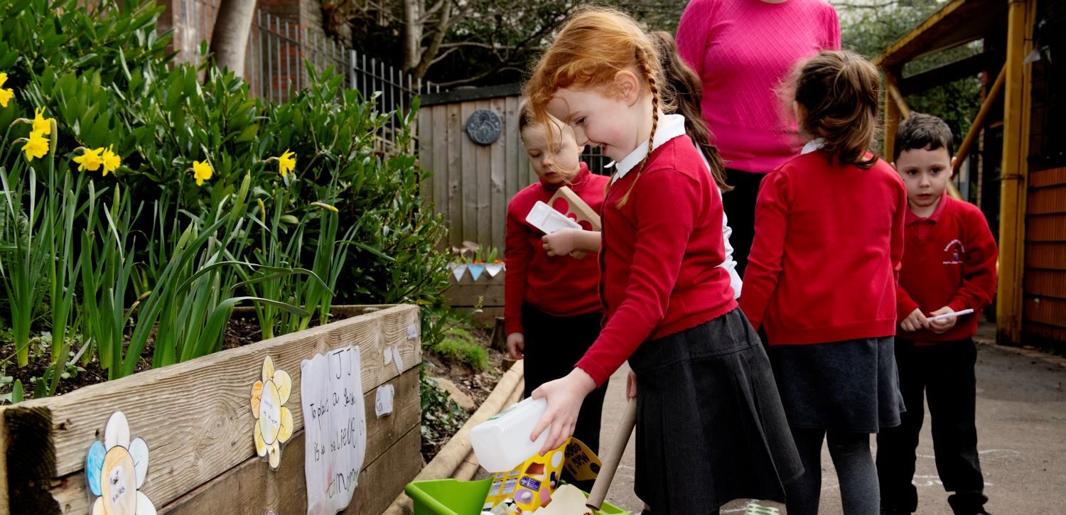 Tri dysgwr yn dyfrio planhigion, yn gwisgo gwisg crys chwys coch.