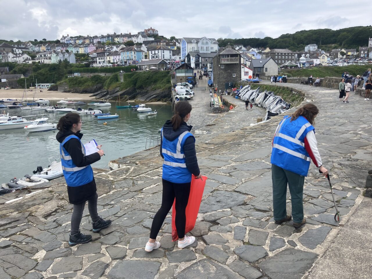 Three volunteers walking along mariner litter picking wearing blue hi-vis vests