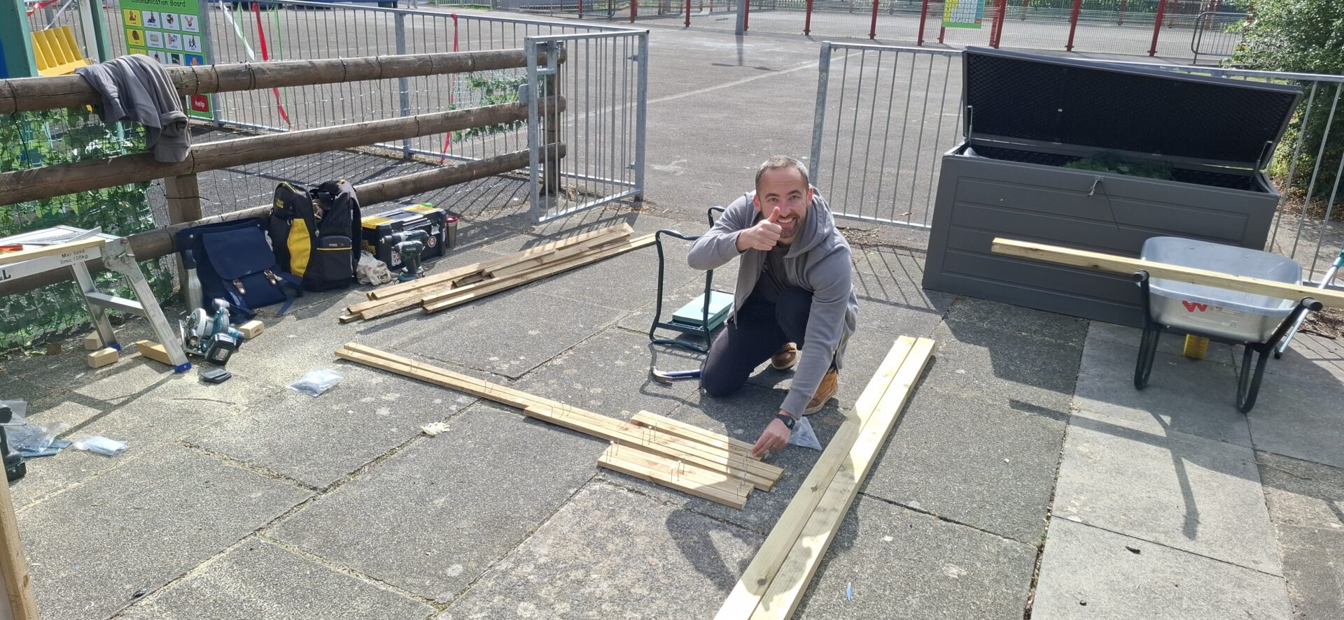 Person yn yr awyr agored gyda'i fawd i fyny, maen nhw'n dal sgriw mewn paledi pren.