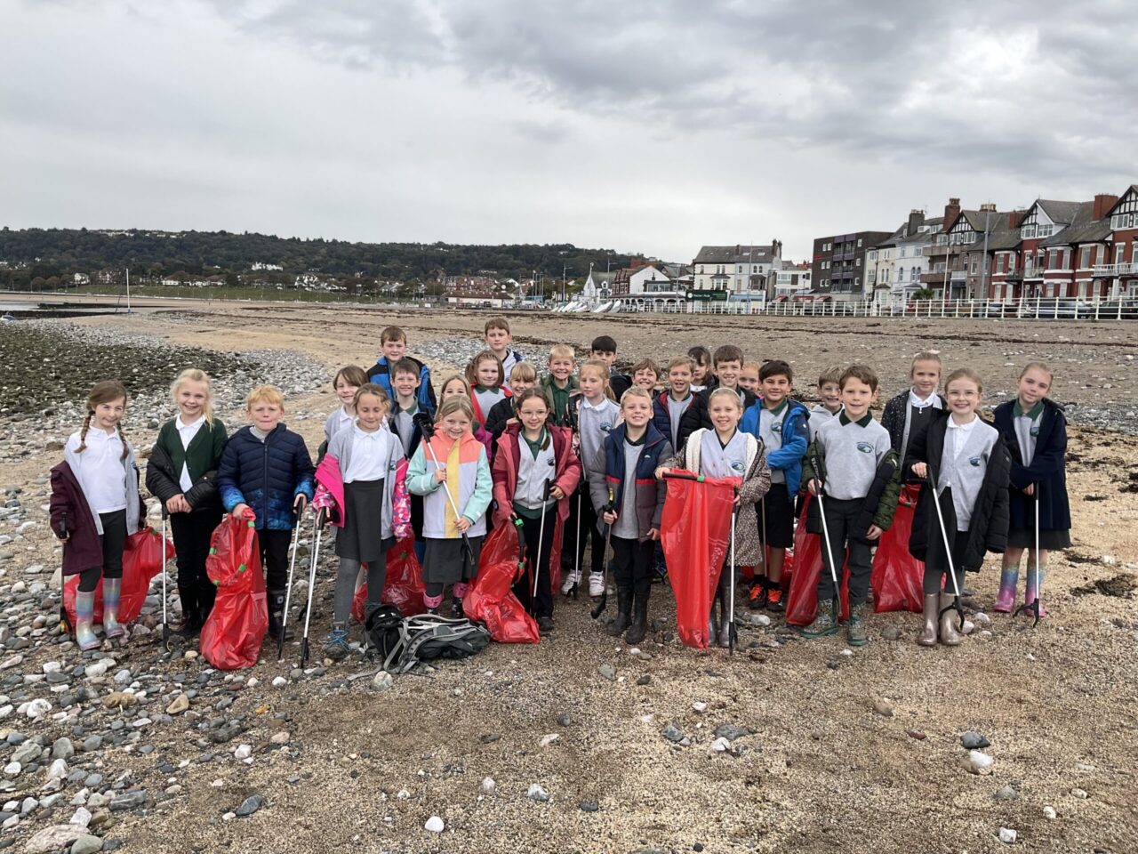 Grŵp o bobl ifanc ar draeth yn dal offer casglu sbwriel.