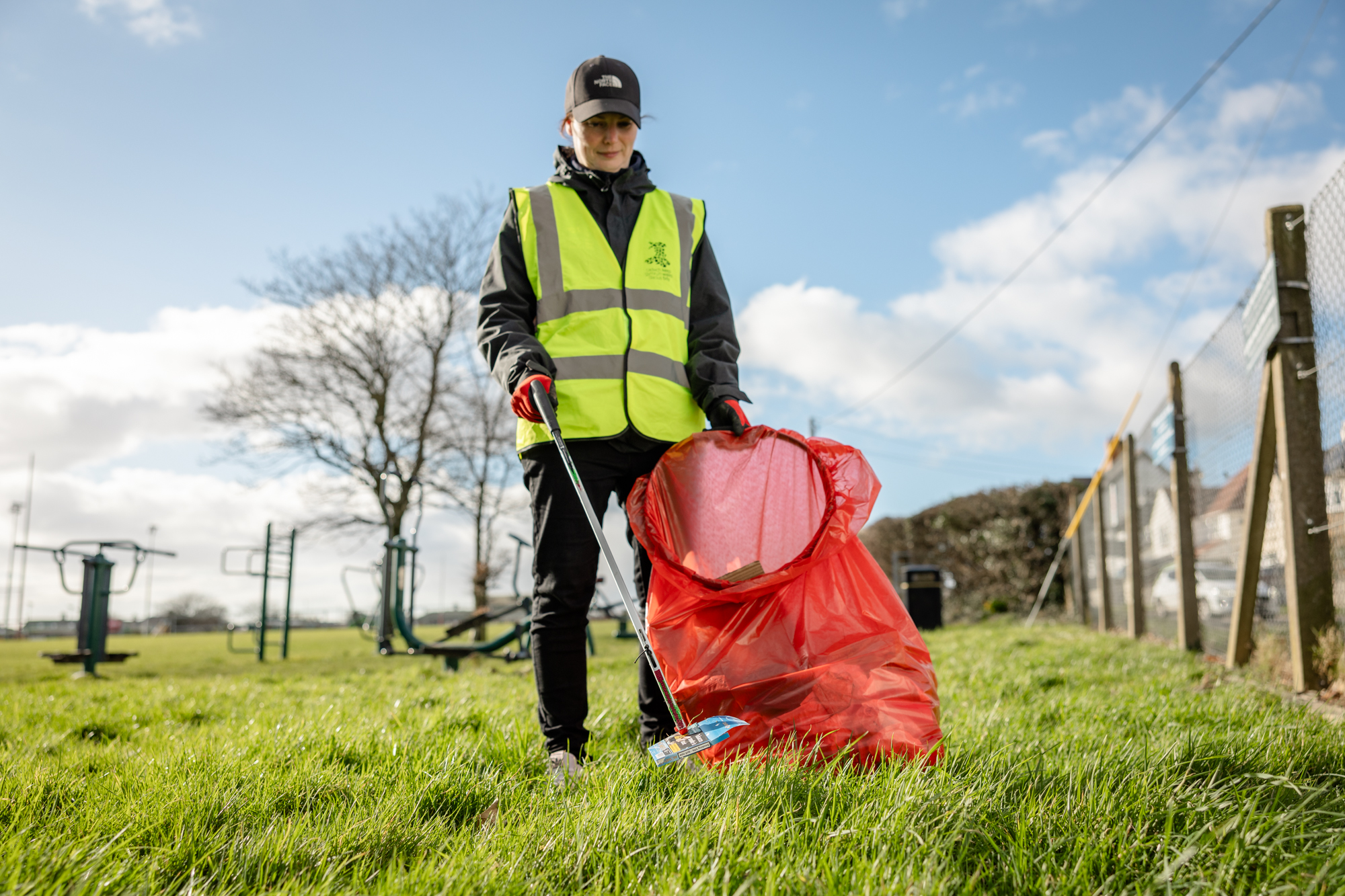 A Litter Champion outside picking up litter in a grassy area on a sunny day