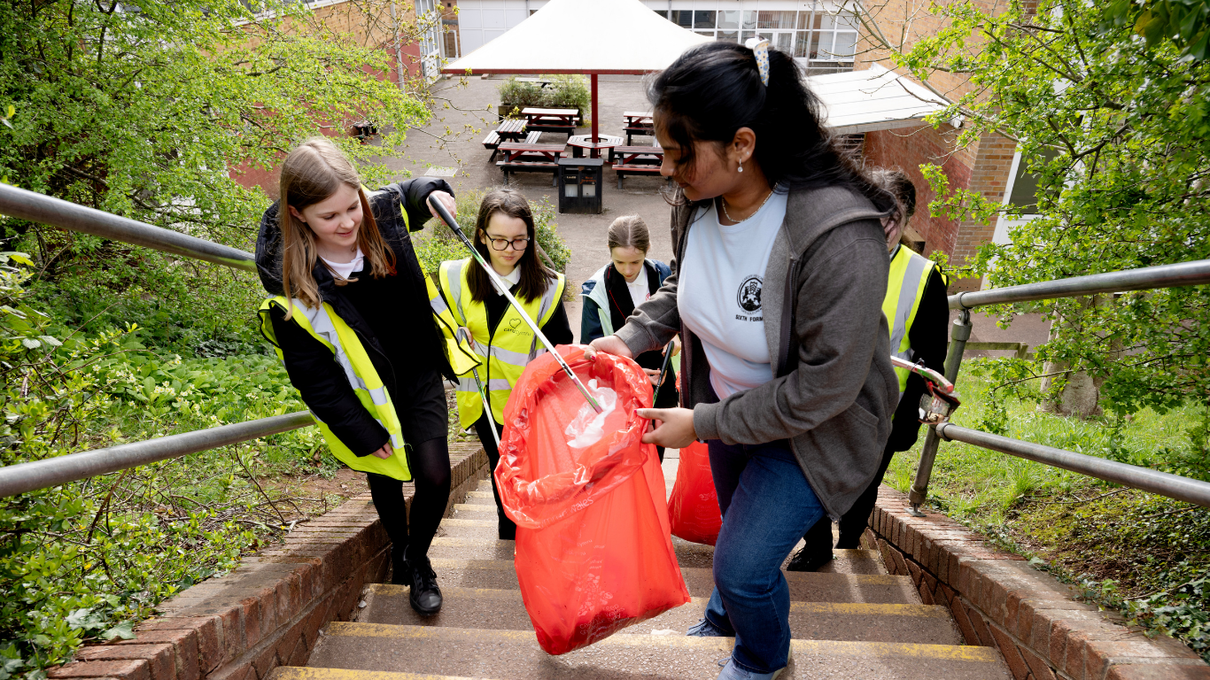 A group of learners in high-visibility vests are walking up a set of stairs, carrying large red bags collecting litter.