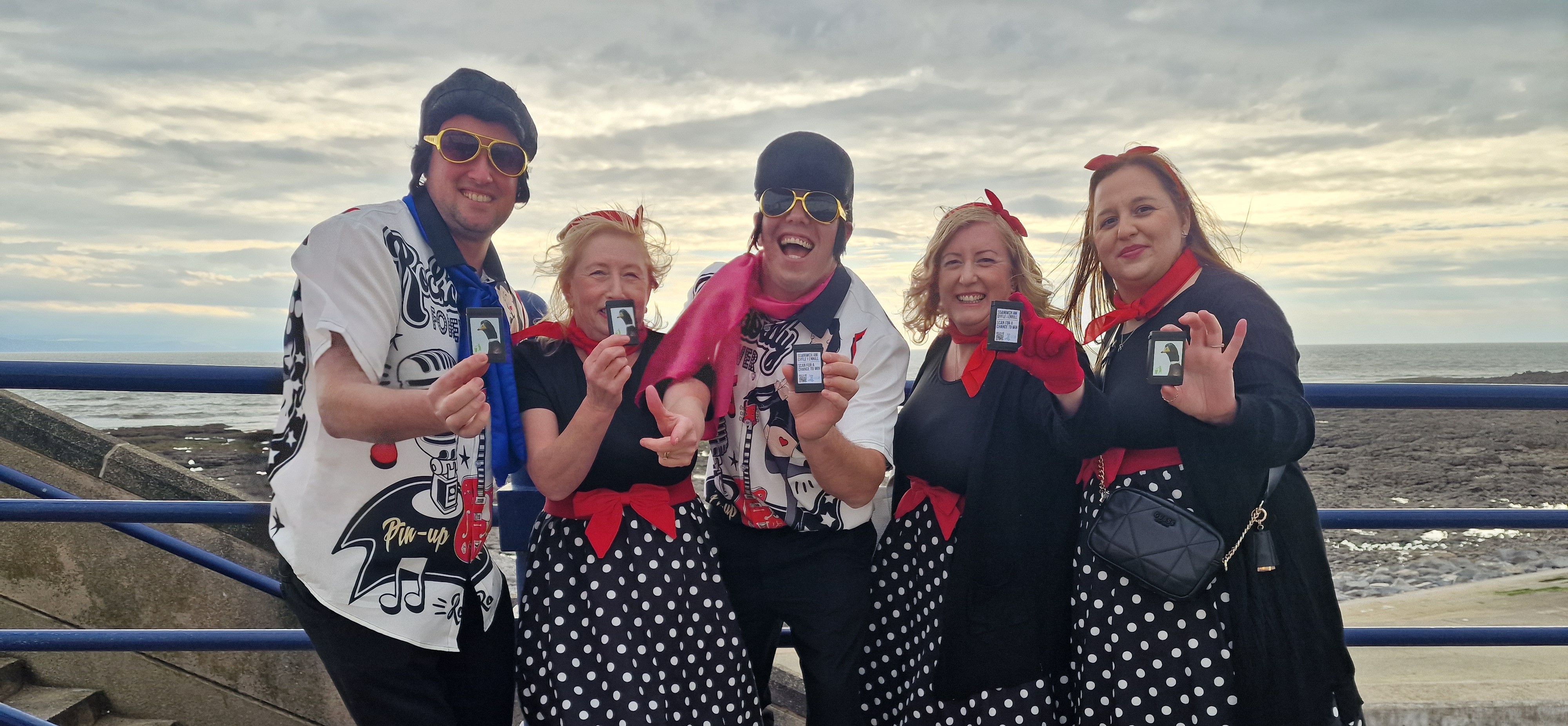 Five people standing on a promenade holding 'Box your Butts' anti-litter campaign boxes in Elvis costumes