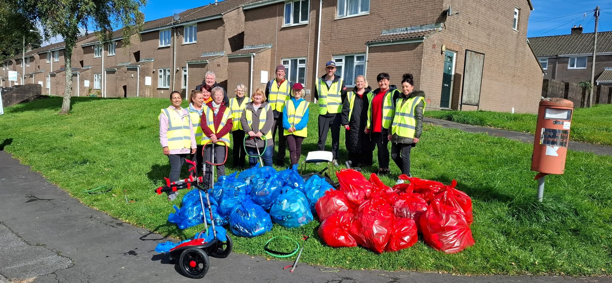 A group of volunteers on a grass banking in front of houses, smiling with red and blue litter bags in the foreground.