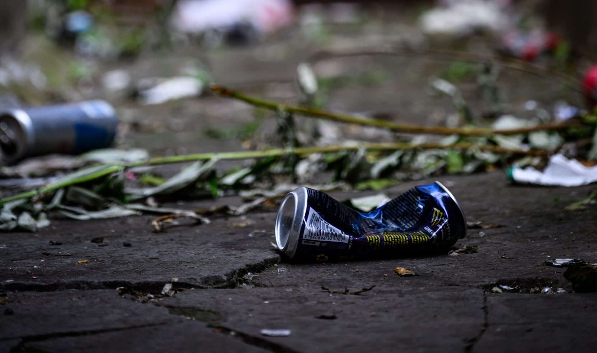 A squashed drinks can discarded on a street. More litter and detritus can be seen in the background.