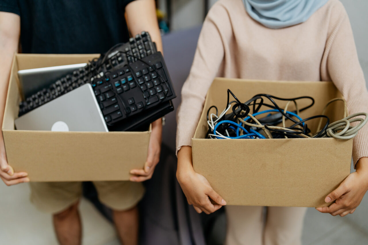 Two people carrying boxes of unused computer equipment for recycling