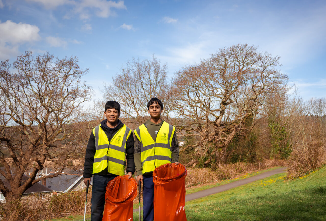 Dau berson yn sefyll ar gae yn dal bagiau coch.