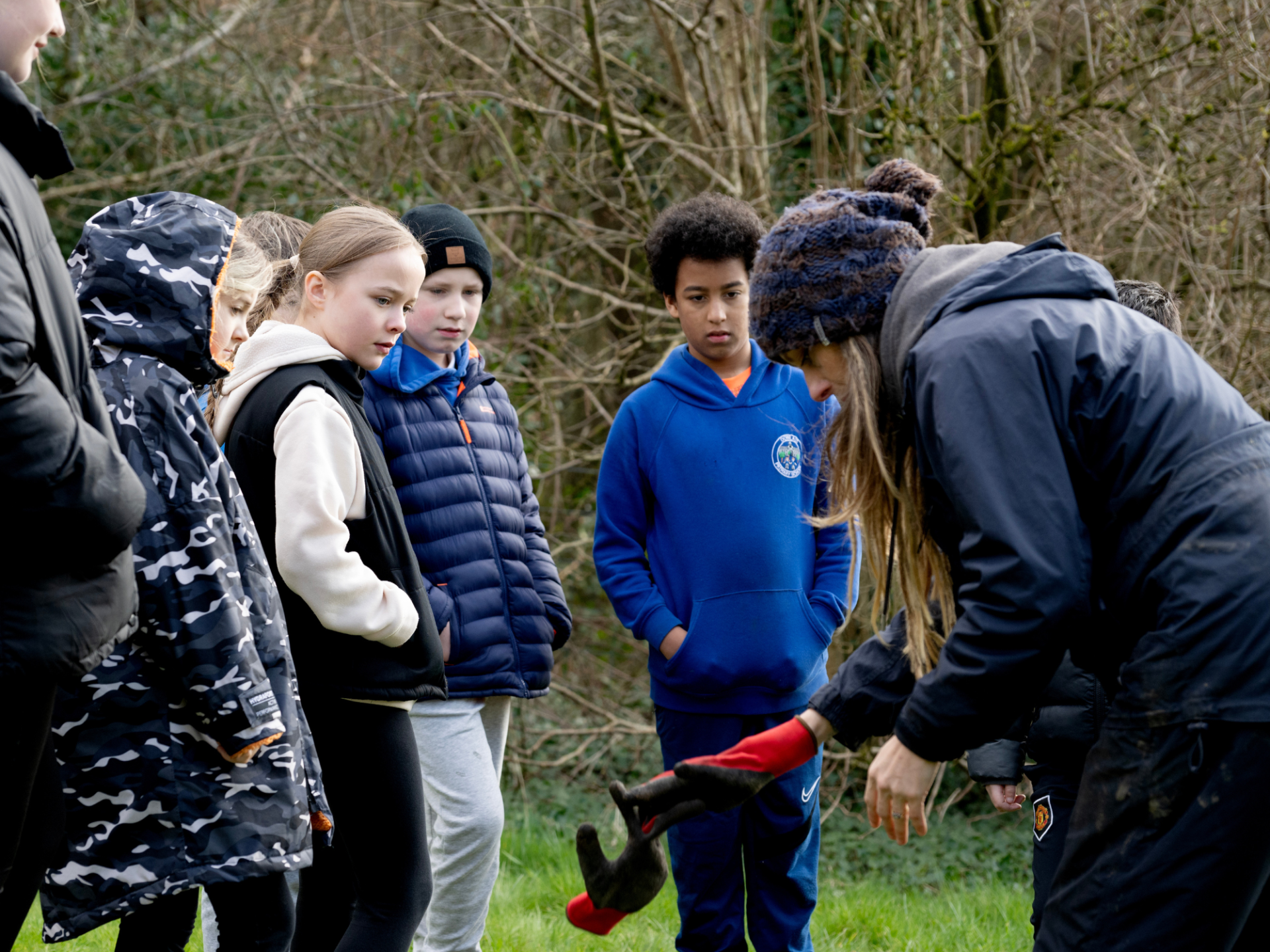 A group of people gathered outdoors, with one person in the foreground showing gloves to a group of children.