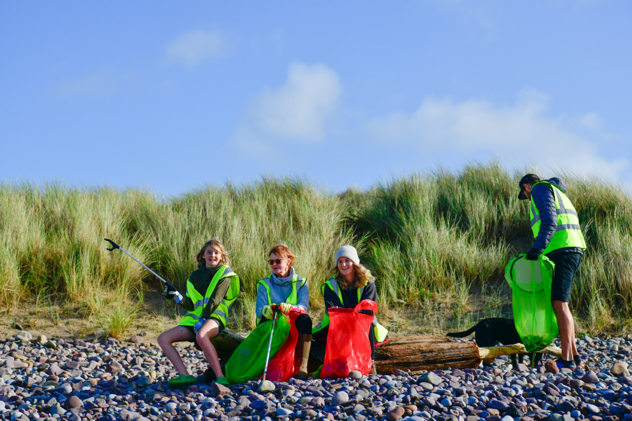 Tri pherson yn gwisgo ei festiau vis yn eistedd ar foncyff.